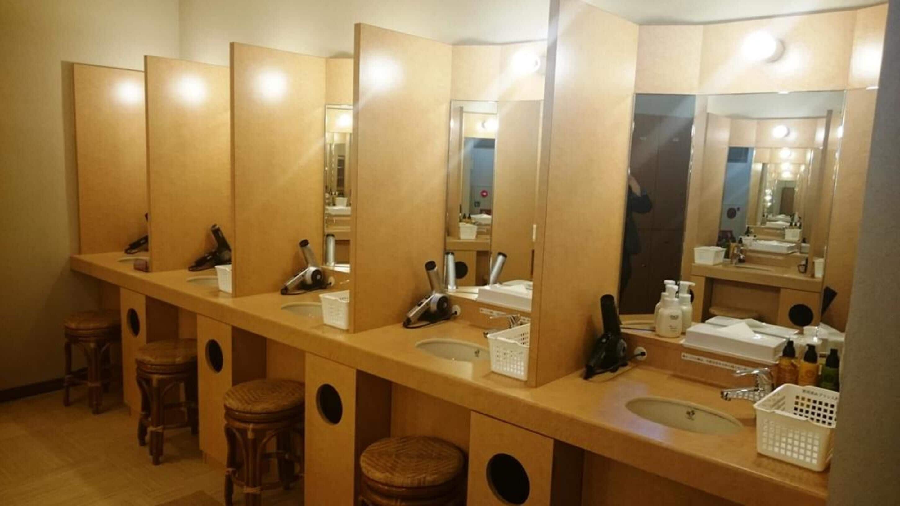 A row of wooden sinks with mirrors, stools, and toiletries in a public restroom.