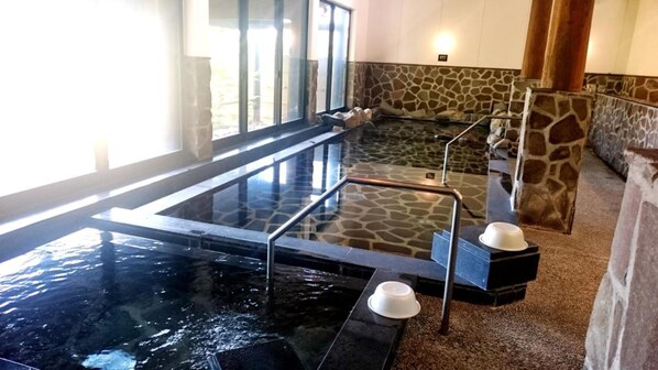Un área de spa con un jacuzzi de vidrio, paredes de piedra y una zona de estar con cojines.