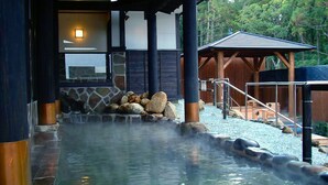 Un onsen japonés tradicional con pared de piedra, pilares de madera y una estructura de madera con techo de tejas.