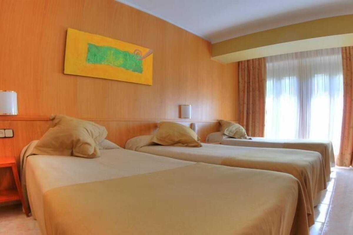 Una habitación de hotel con dos camas, un cuadro en la pared y una ventana con cortinas.