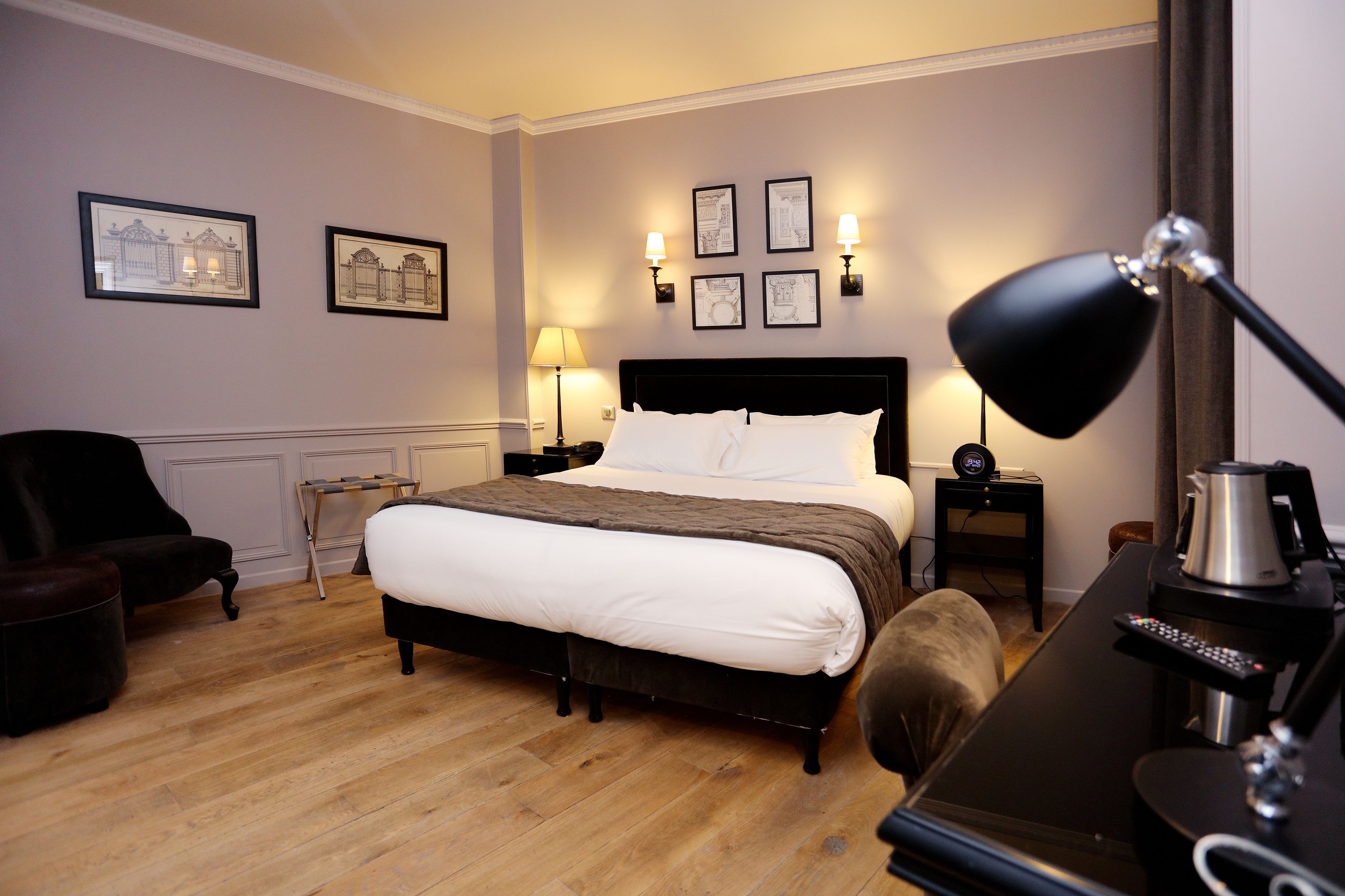A hotel room with a large bed, a desk with a lamp, a chair, and framed pictures on the wall.