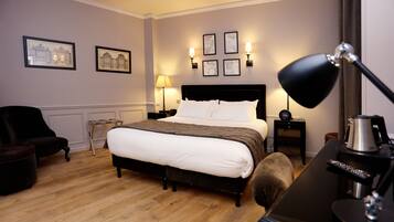 Habitación de hotel con una cama grande, un escritorio con lámpara, una silla y cuadros en la pared.
