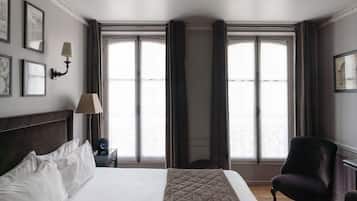 Habitación de hotel con una cama grande, una silla, una mesita de noche con lámpara y una ventana con cortinas.