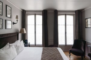 A hotel room with a large bed, a chair, a nightstand with a lamp, and a window with curtains.