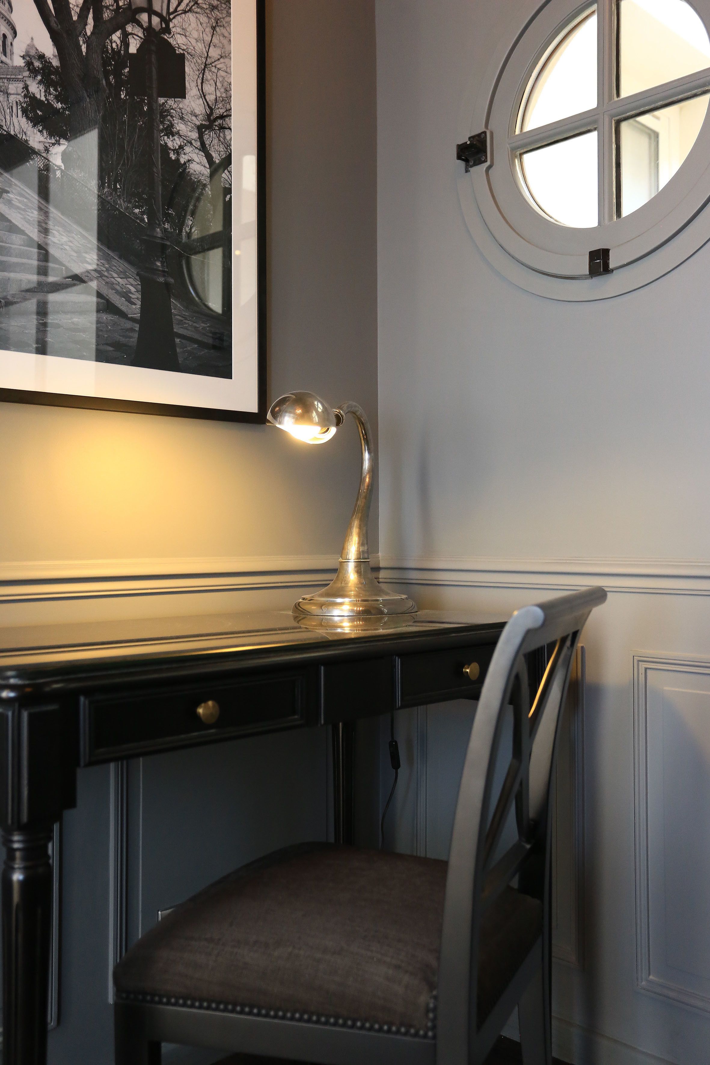 A desk with a lamp, a chair, and a round window.