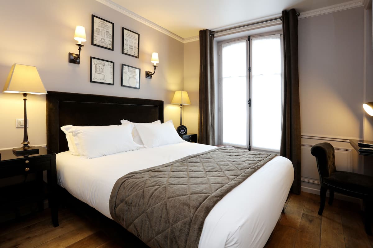 Una cama bien hecha con una colcha acolchada, dos lámparas de noche, una mesita y una silla.
