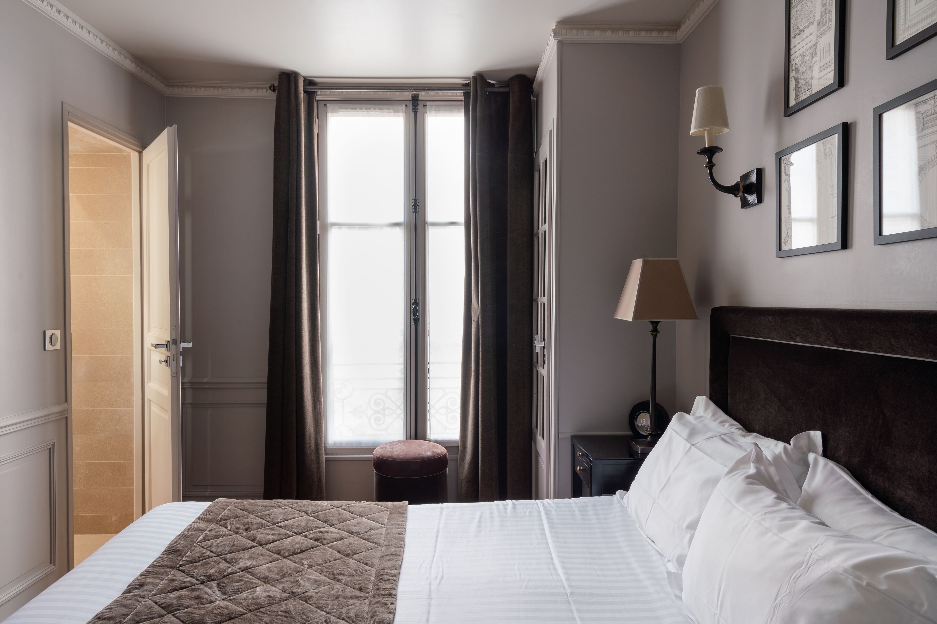 Una camera d'albergo con un letto, un comodino con una lampada, una finestra con tende e quadri appesi al muro.