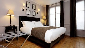 A neatly made bed with a dark headboard, two bedside lamps, and a window with curtains.