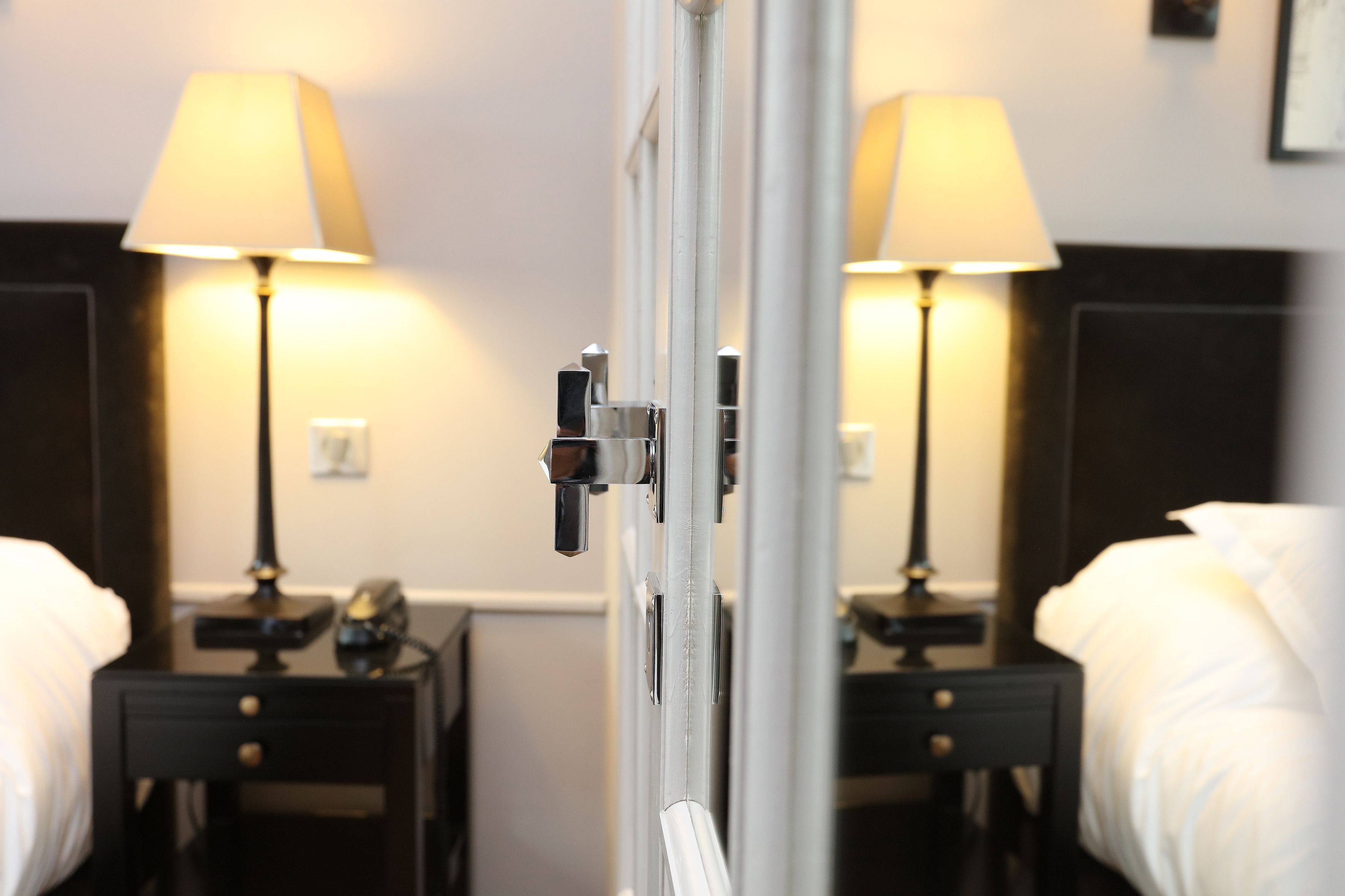 A hotel room with a bed, a nightstand, a lamp, and a mirror.