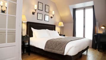 A neatly made bed with a dark headboard, two bedside tables with lamps, a large window with curtains, and framed pictures on the wall.