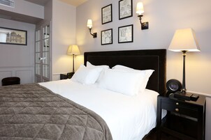 A neatly made bed with white linens and a quilted blanket, a bedside table with a lamp, and framed pictures on the wall.