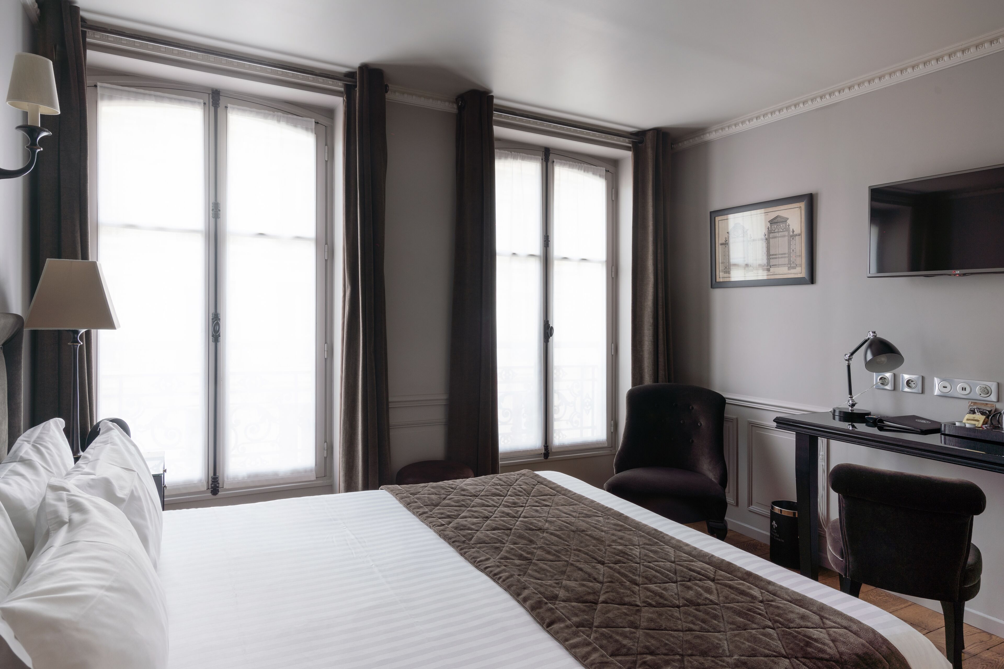 A hotel room with a large bed, a desk with a chair, a TV, and a window with curtains.