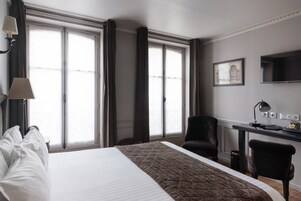 A hotel room with a large bed, a desk with a chair, a TV, and a window with curtains.