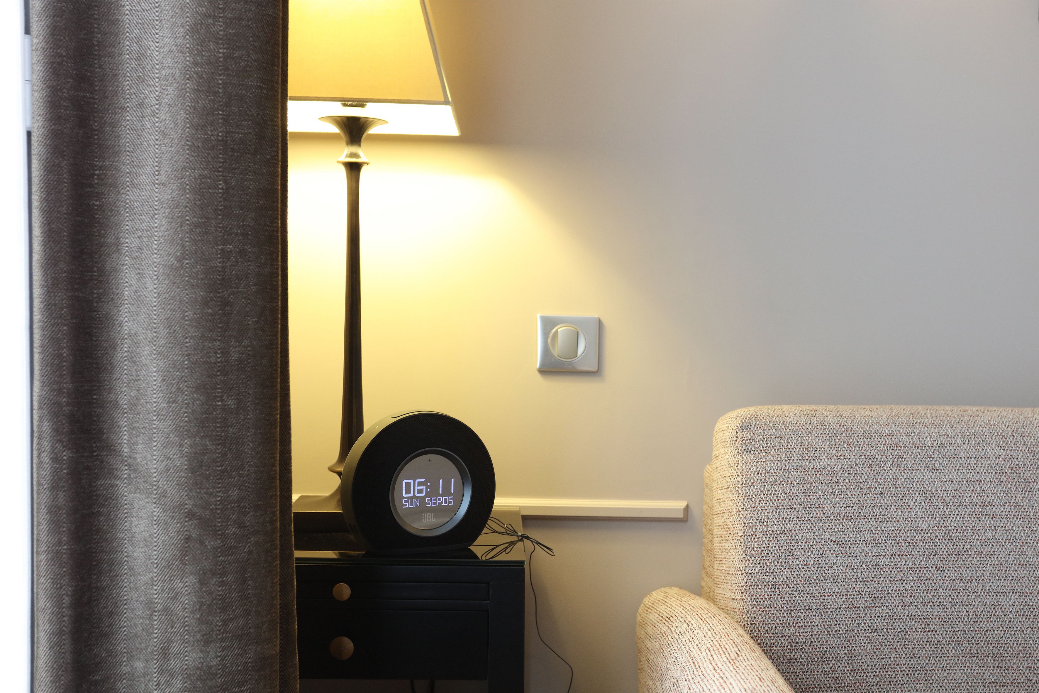 A room with a bed, a nightstand with a clock, a lamp, and a chair.