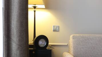 A room with a bed, a nightstand with a clock, a lamp, and a chair.