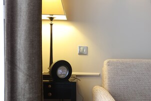 A room with a bed, a nightstand with a clock, a lamp, and a chair.