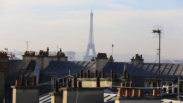 Une vue de la Tour Eiffel depuis un toit surmonté de nombreuses cheminées et d’antennes.