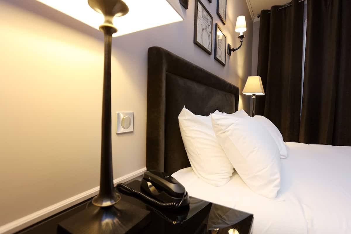 Una habitación de hotel con una cama grande, un teléfono en la mesita de noche, una mesita auxiliar y una lámpara de pared.