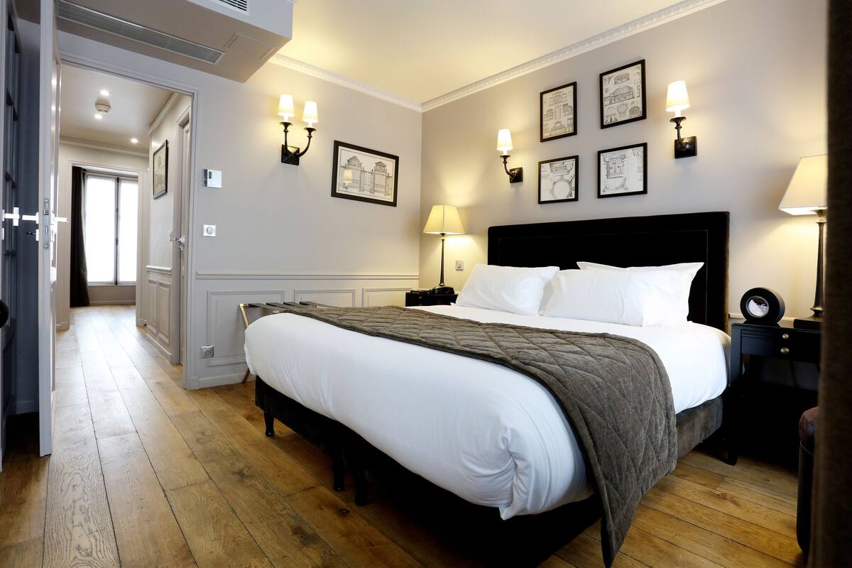Una habitación de hotel con una cama grande, lámparas de noche, una mesita de noche y cuadros en las paredes.