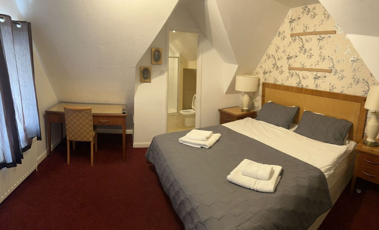 A hotel room with a bed, a desk, a chair, a nightstand, and a bathroom.