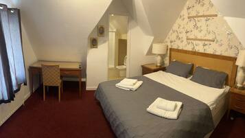 A hotel room with a bed, a desk, a chair, a nightstand, and a bathroom.