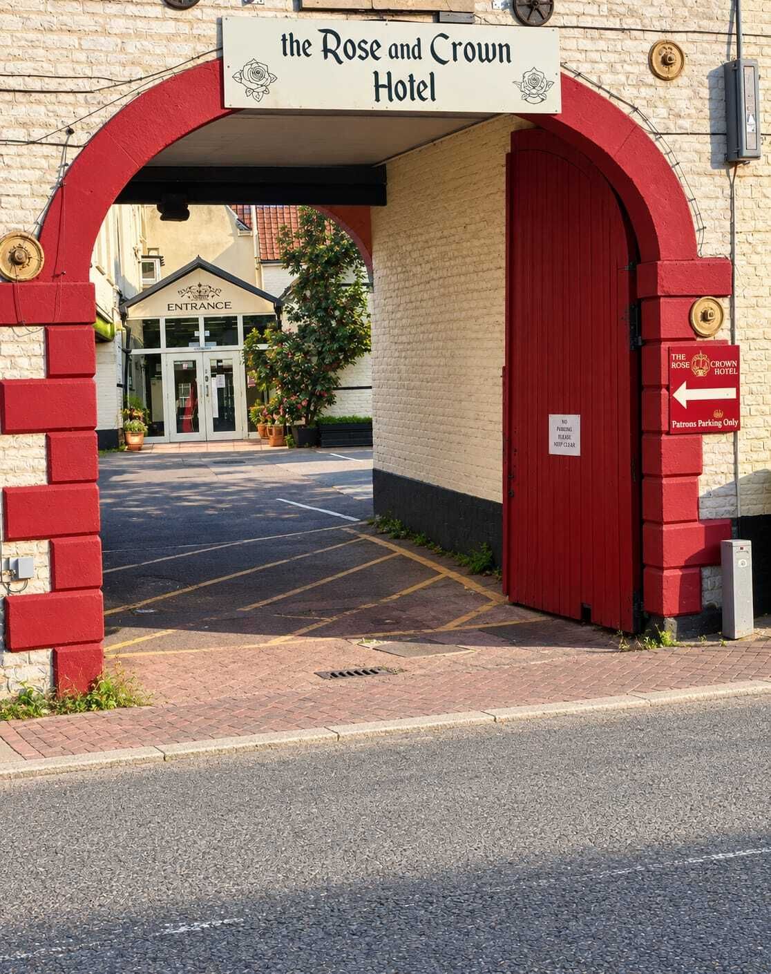 A entrada do Hotel Rose and Crown, com um arco vermelho e uma placa indicando 'Estacionamento para Clientes'.