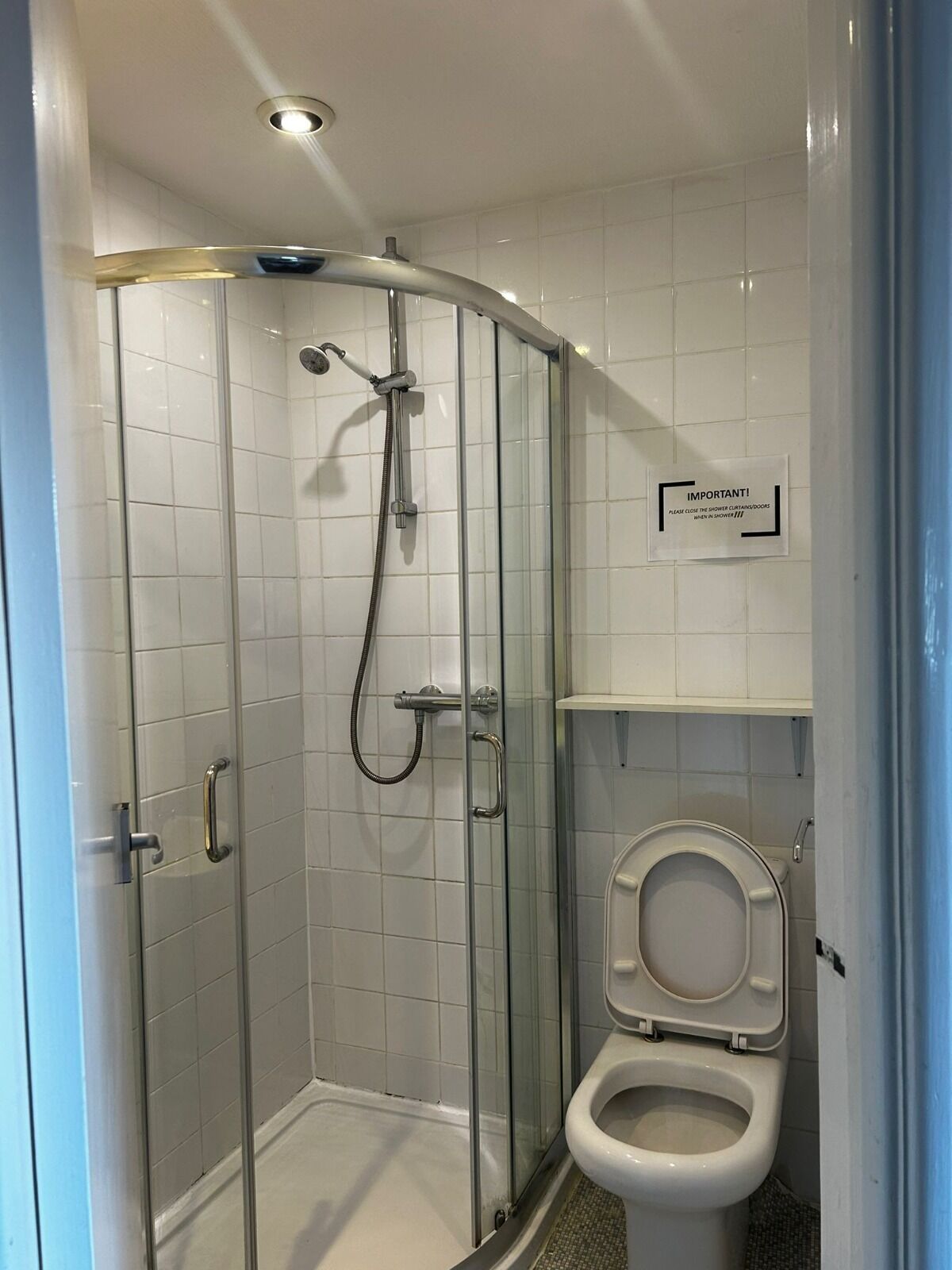 A modern bathroom with a glass-enclosed shower, a toilet, and a sign instructing to close the shower curtains.
