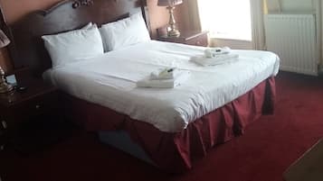Ein ordentlich bezogenes Bett mit weißen Leinentüchern, einem hölzernen Kopfteil und einem roten Teppichboden.