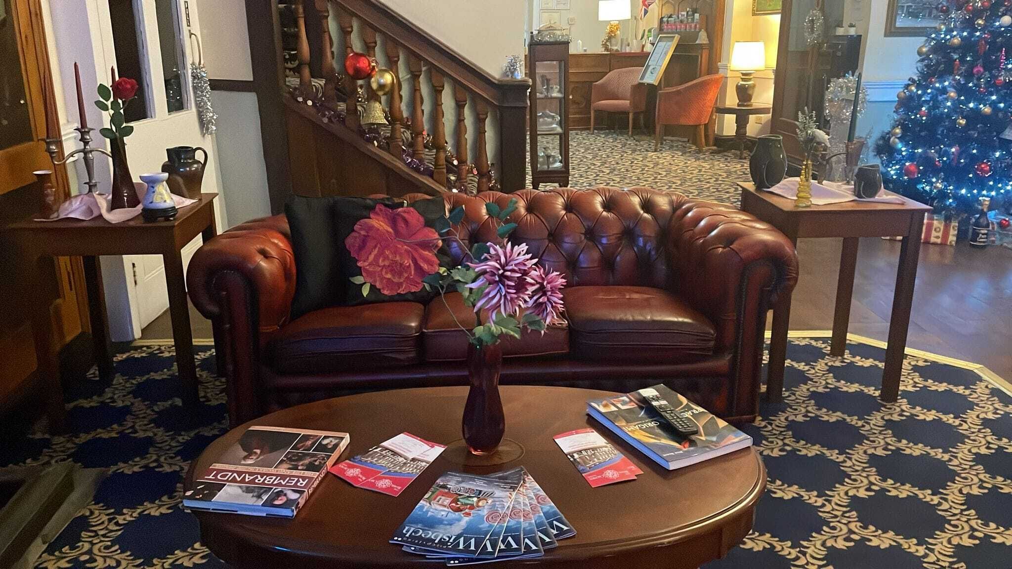 Un sofá de cuero con un jarrón de flores, una mesa de centro con revistas y un árbol de Navidad en una habitación con luz cálida.