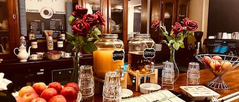 A coffee station with a menu, jars labeled with beverages, and a bowl of apples.