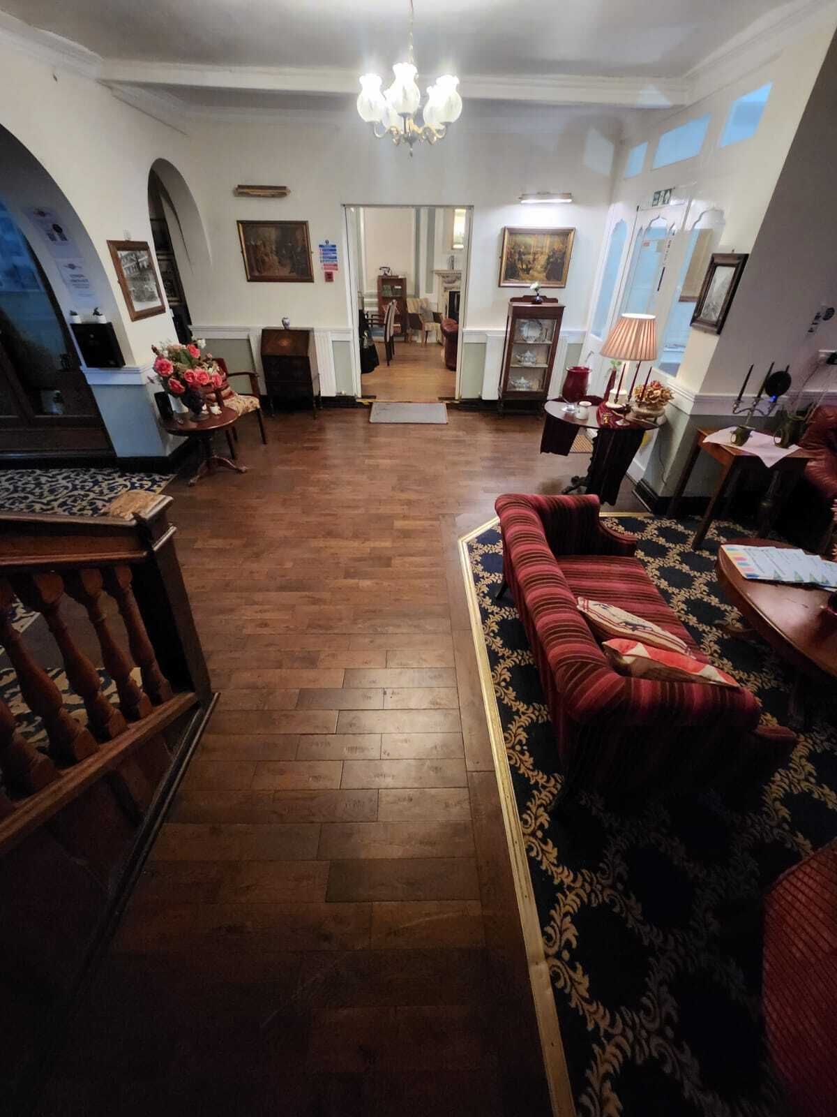 Ampla sala de estar com piso de madeira, um sofá vermelho, um lustre e vista para a sala de jantar.