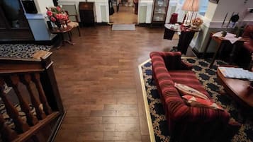 Ampla sala de estar com piso de madeira, um sofá vermelho, um lustre e vista para a sala de jantar.