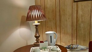 A wooden side table with a lamp, a coffee pot, and a tray with teacups and saucers. - The Rose and Crown Hotel (Wisbech)