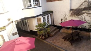 A courtyard with a reception desk, wooden benches, and potted plants. - The Rose and Crown Hotel (Wisbech)