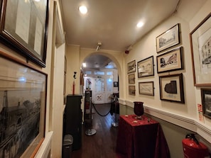 A corridor with framed pictures on the walls, a red table with a vase, and a fire extinguisher. - The Rose and Crown Hotel (Wisbech)