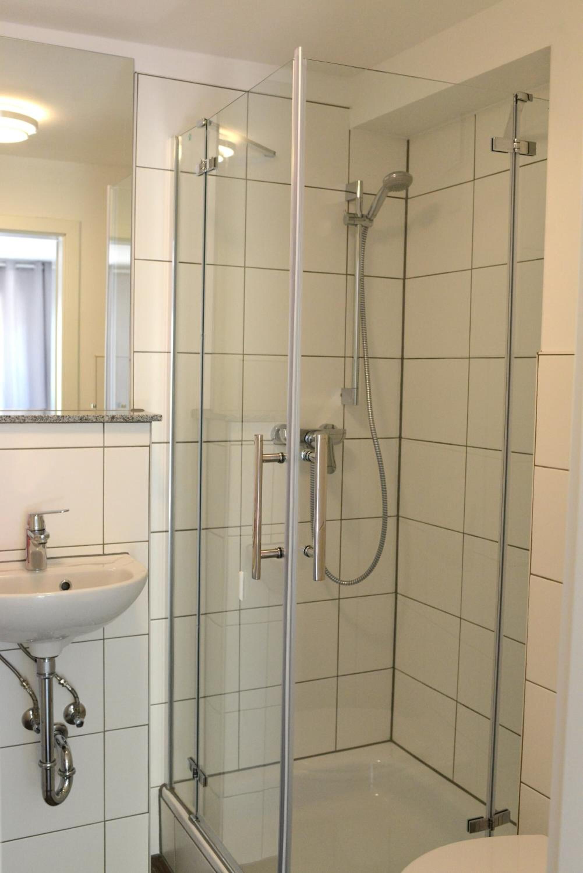Un baño moderno con ducha de vidrio, lavamanos y espejo.