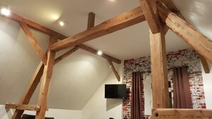 Une pièce avec des poutres apparentes, un mur en briques et un téléviseur fixé au mur.