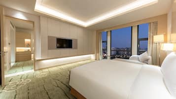 Habitación de hotel con una cama grande, un televisor de pantalla plana montado en la pared, vista a la ciudad a través de amplios ventanales y un baño separado.
