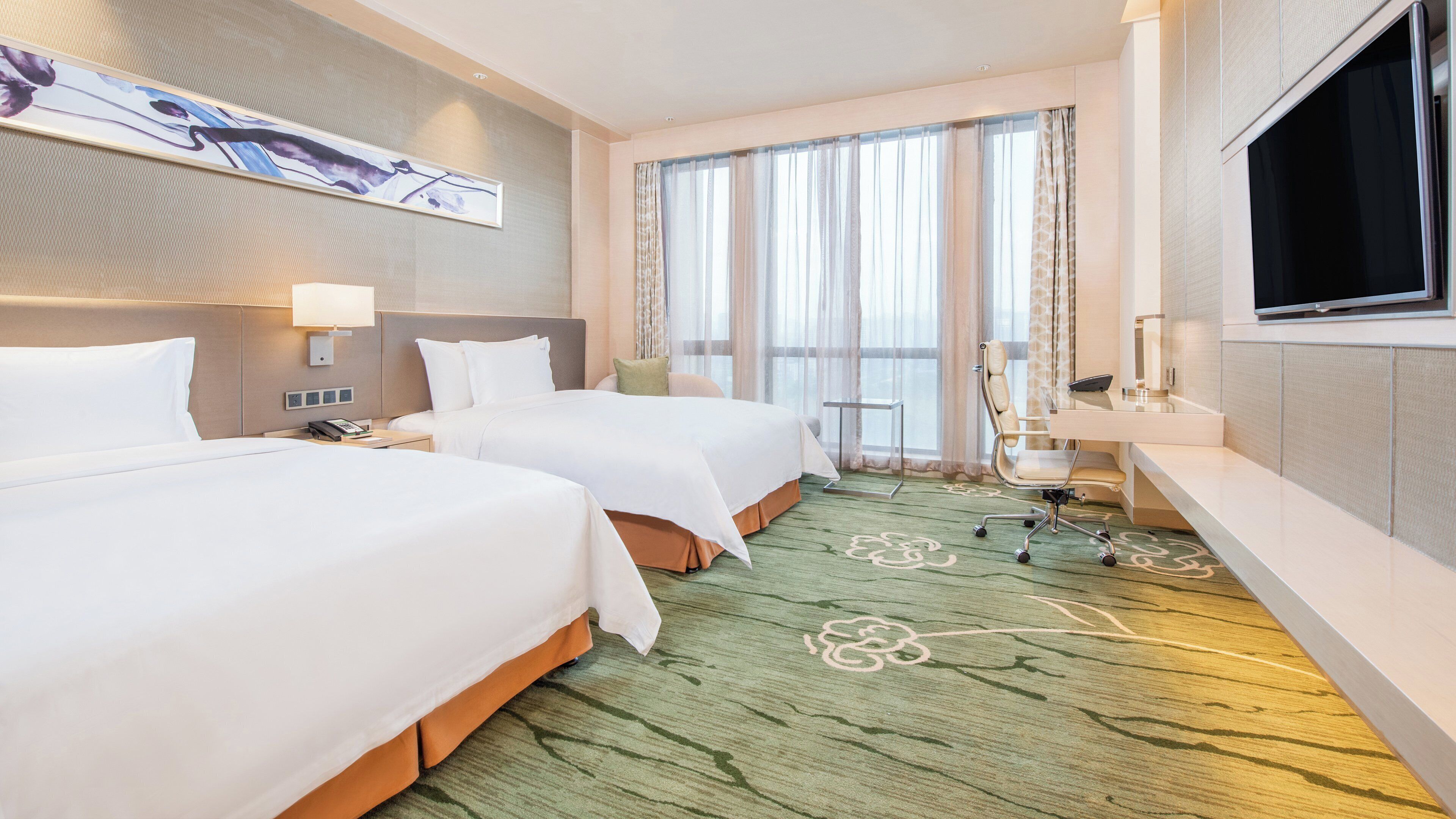 Habitación de hotel con dos camas, un escritorio con silla, televisión y un ventanal con cortinas.