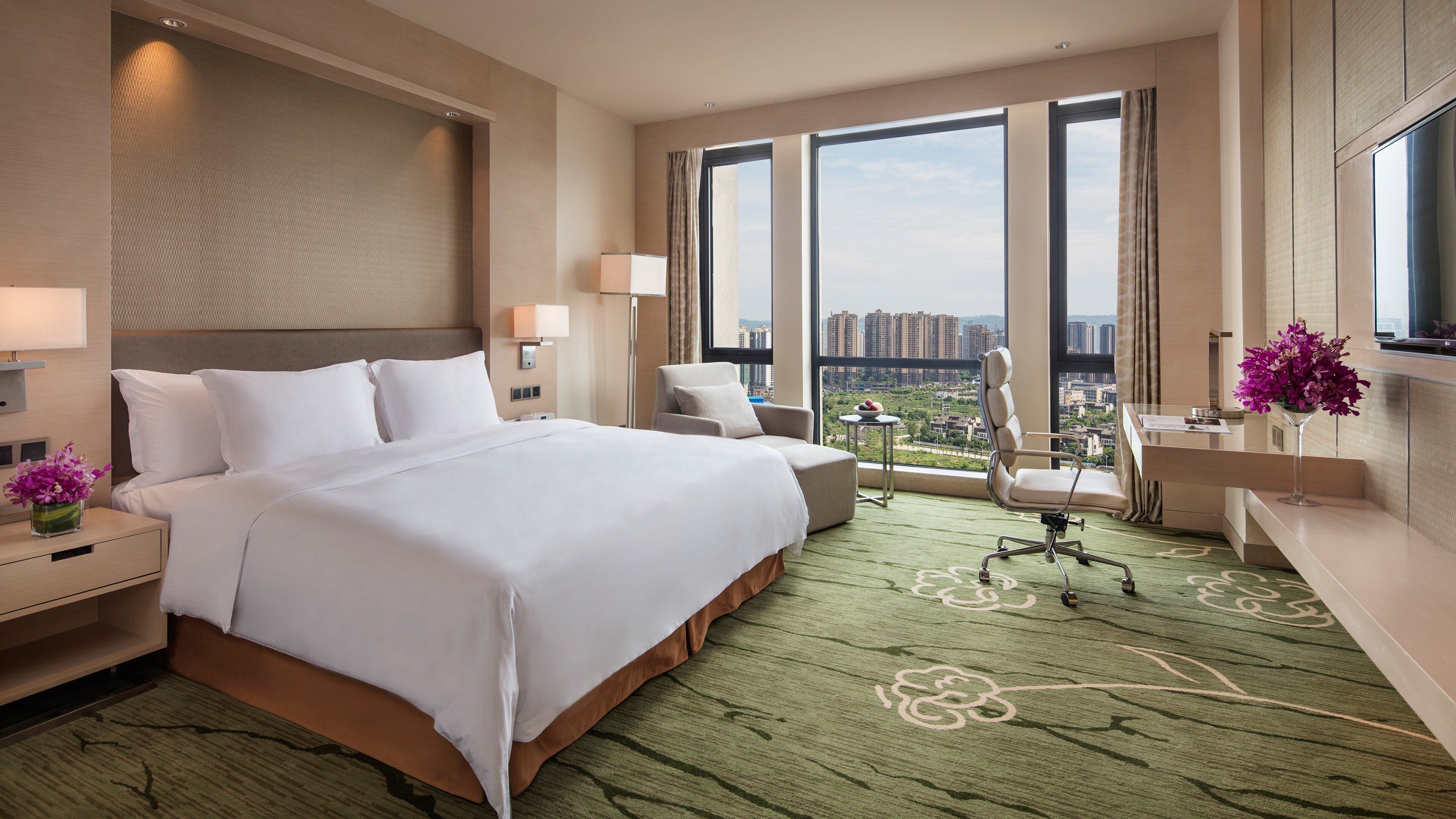 Habitación de hotel con una cama grande, un escritorio, una silla, televisión y vistas a la ciudad.