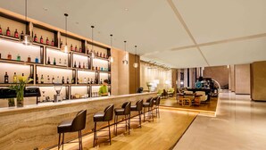 Un espace bar doté d’un comptoir en marbre, de nombreuses bouteilles d’alcool et de tabourets de bar.