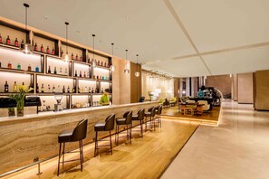 Un espace bar doté d’un comptoir en marbre, de nombreuses bouteilles d’alcool et de tabourets de bar.