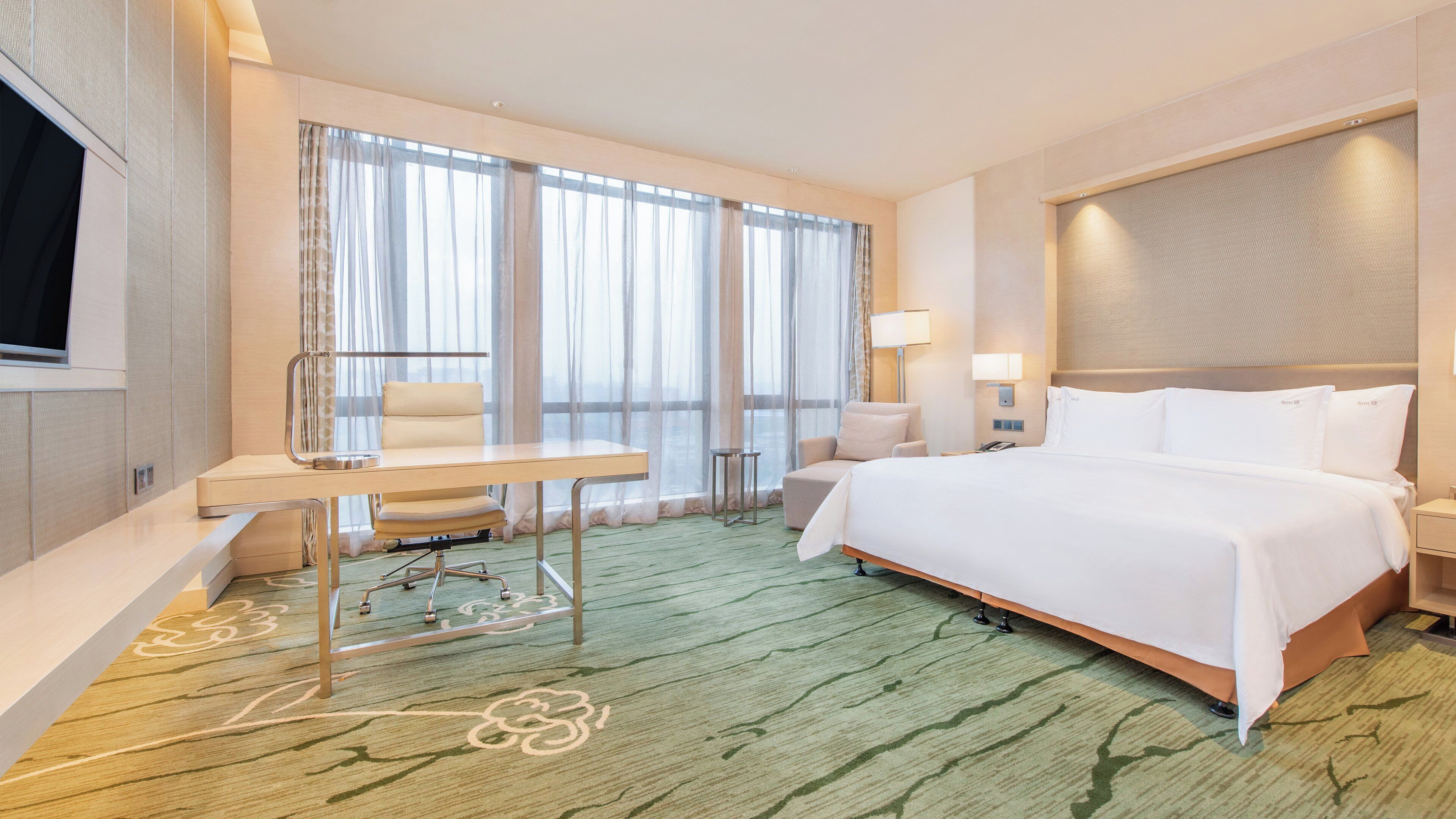 Een hotelkamer met een bed, bureau, stoel en grote ramen.