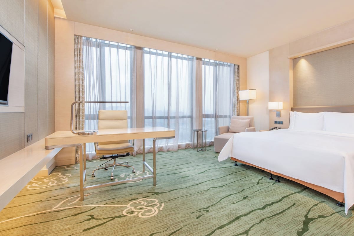 Una habitación de hotel con cama, escritorio, silla y ventanas amplias.