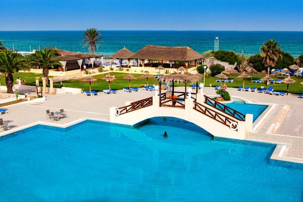 Un resort con una amplia piscina, tumbonas y vista al océano.