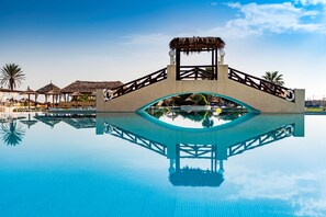 A clear blue pool with a wooden bridge and thatched-roof structures in the background. - El Borj Hotel (Mahdia)