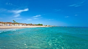 Une plage avec une eau turquoise et limpide, des parasols et des chaises de plage.