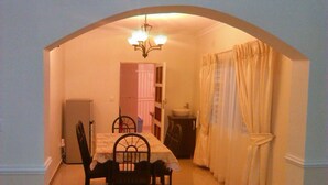 A dining area with a table and chairs, a chandelier, and a view through an archway to a bathroom. - Home Up Guest House (Blantyre)