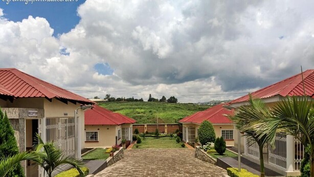 A hotel entrance with a paved pathway leading to reception, surrounded by greenery and red-roofed buildings. - Home Up Guest House (Blantyre)
