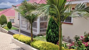 A residential area with houses featuring red roofs, a gated entrance, and well-maintained gardens with various plants and flowers. - Home Up Guest House (Blantyre)